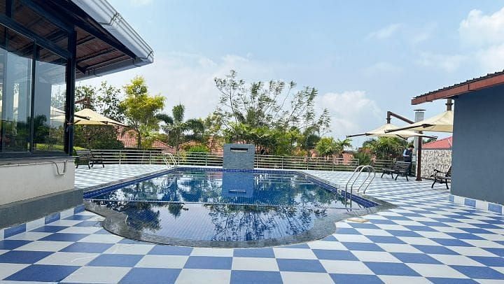 A serene pool area at Woodstock Resorts, Coorg featuring a checkered tile pattern and surrounding greenery.