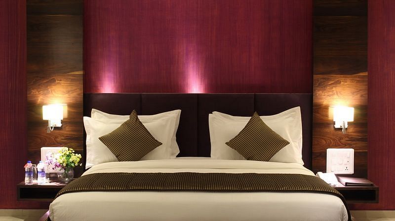 A room showcases a king size bed with a dark purple headboard, bedside tables with lamps, and elegant bedding.