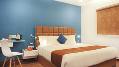 A King bed with a study table and side tables next to it inside the Deluxe King Room - VITS Select, Rajkot.