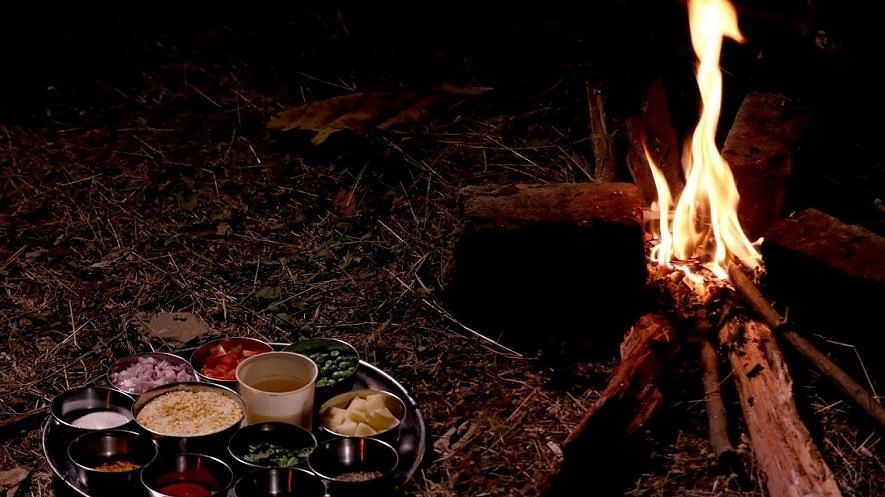 Jungle Cooking - Sajan - a thali meal of 10 items placed on the grass beside a camp fire.