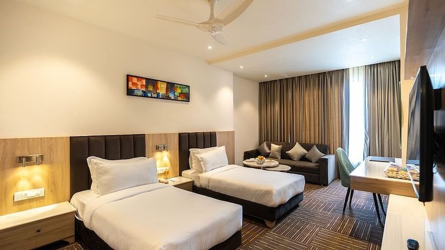 Bright twin-bed hotel room with full-length curtains, work desk, and a comfortable lounge sofa at Clarks Inn Express, Ayodhya.
