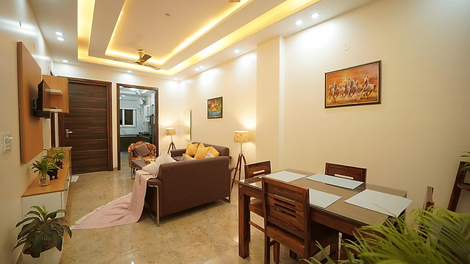 Lounge and dining area of Lime Tree Hotels & Service Apartment Private Limited featuring a brown sofa, a dining table, and a wall mounted television.