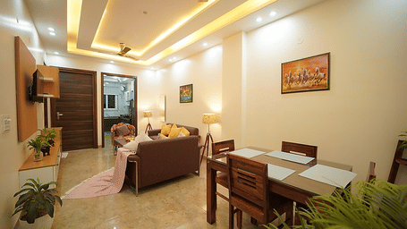 Lounge and dining area of Lime Tree Hotels & Service Apartment Private Limited featuring a brown sofa, a dining table, and a wall mounted television.