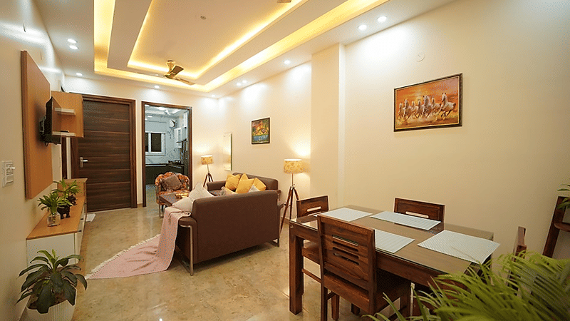 Lounge and dining area of Lime Tree Hotels & Service Apartment Private Limited featuring a brown sofa, a dining table, and a wall mounted television.