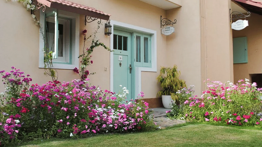 Exterior view of Karma Chalets showing flowering plants, green lawn, and cream-colored building with red-tiled roof.