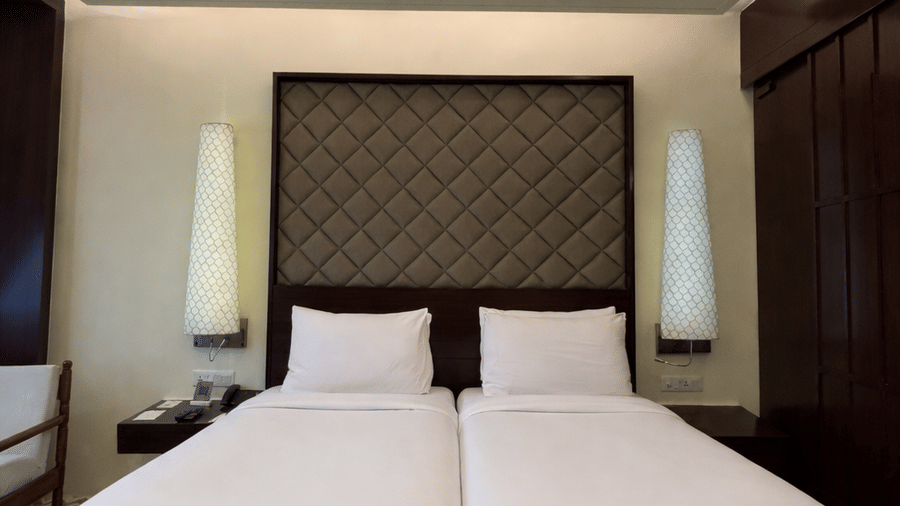 Twin beds with tall, patterned headboards and white linens beneath a ceiling fan in the Superior Twin room at Clarks Amer, Jaipur.