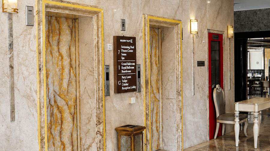 Hotel elevator lobby at Golden Tulip Kukas Jaipur with marble wall cladding, lift doors, and soft ambient lighting.