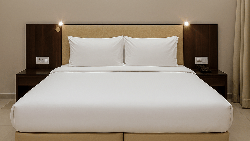 A centred view of a double bed at the Superior Room in Tropicana Resort & Spa, Alibaug, featuring bedding, a sleek dark wood headboard, and built-in bedside reading lights.