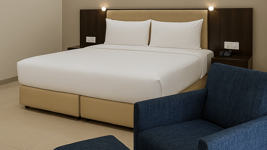 Superior Room at Tropicana Resort & Spa, Alibaug, featuring a large bed with crisp white linens and a tan base, positioned next to a plush navy blue armchair.