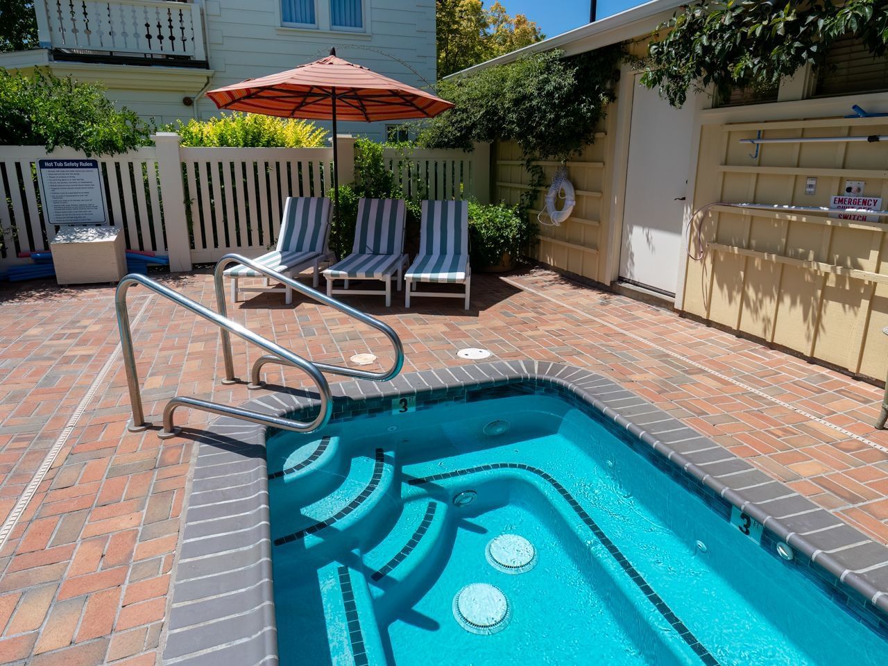 A refreshing outdoor swimming pool with comfortable lounge chairs and a vibrant red umbrella by the water at The Tallman Hotel.