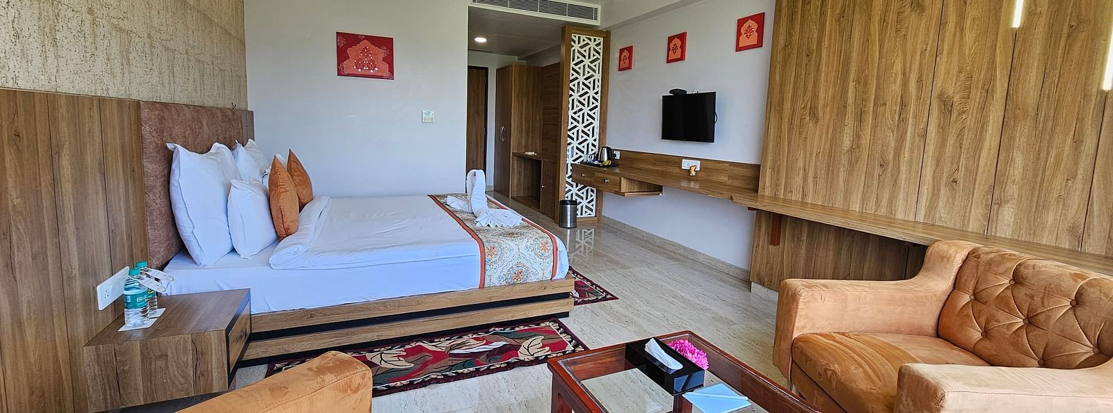 An wider shot of a room at Bamboo Saa Mulberry Resort, with a bed, seating area, a television, and a decorative rug.