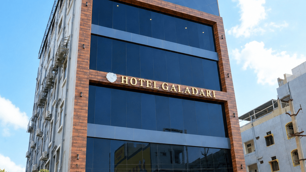 Exterior of the multistory Hotel Galadari building featuring a glass facade and landscaped entrance steps under a blue sky.
