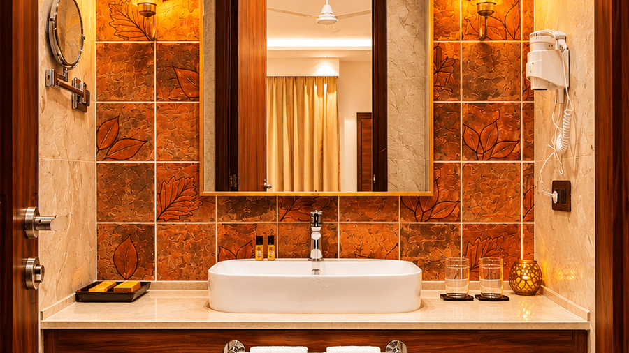 Bathroom with terracotta-tiled walls, a mirror, wall sconces, and folded towels at Kadamb Kuteer, Vrindavan.