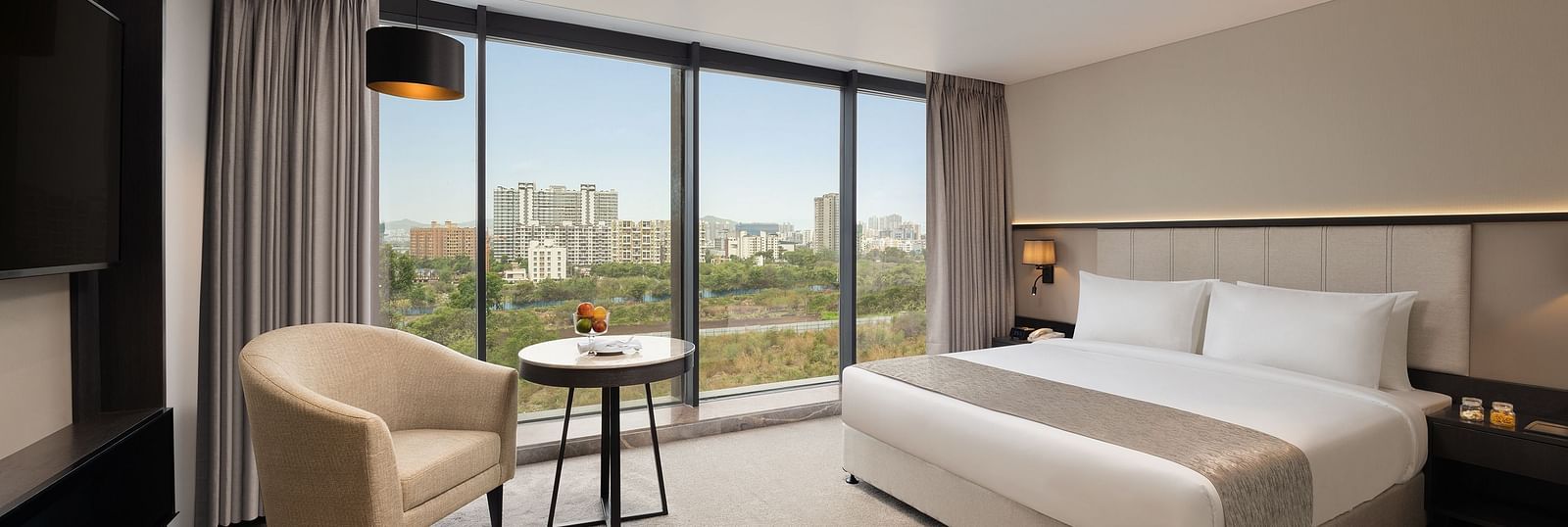  Premier Room with a king size bed and a sofa beside a large window at Essentia Premiere, Pune.