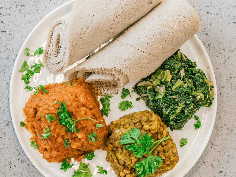 A plate containing injera and three veg side dishes on a patterned surface