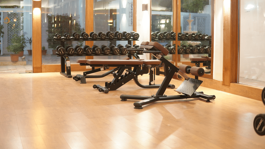 A strength training area with flat benches, dumbbell racks, wall mirrors, and glass partitions at Clarks Avadh, Lucknow.
