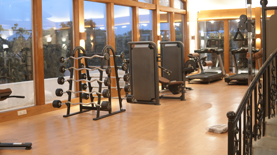 A gym corner with resistance machines, pulley systems, wooden flooring, and full-height windows at Clarks Avadh, Lucknow.
