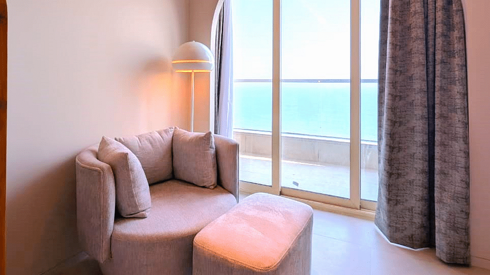 A partial view of a living area at Swosti Premium Beach Resorts, Puri, with a chair and an arched window.