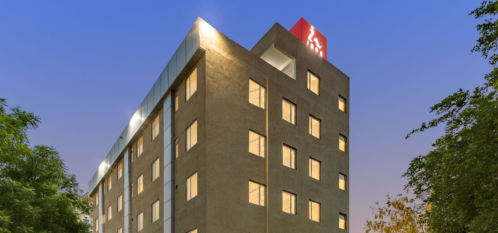 A facade image of a well-lit Inde Cyber City, Gurgaon building and beyond it an evening sky can be seen in the background - Inde Hotels & Resorts