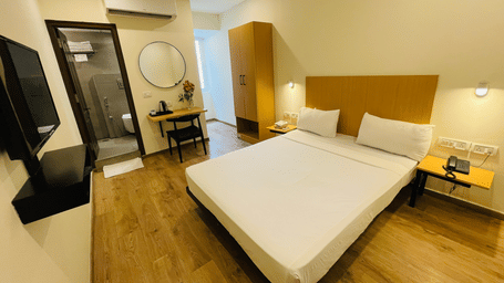 A room at Sanctum Suites, Richmond Road, Bangalore with a double bed, a desk, a round mirror, a wall mounted television, and an A/C.