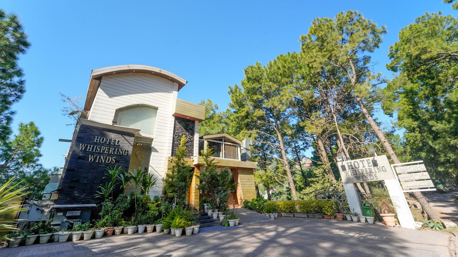 A facade image of DLS Whispering Winds surrounded by trees and greenery