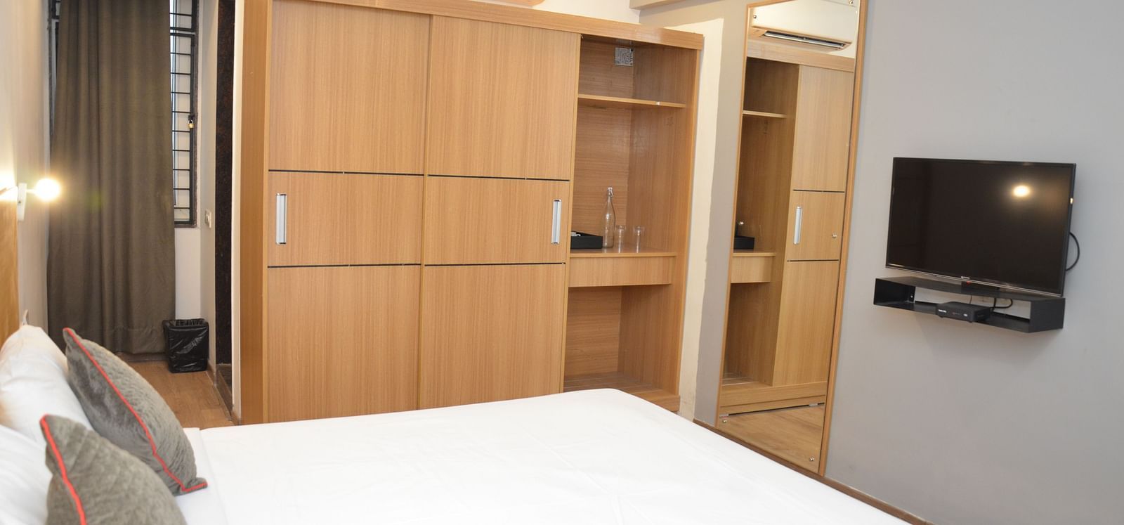 Corner view shot of a bedroom with a double bed, wooden wardrobe, and a television on the wall - Lords Eco Inn Belagavi