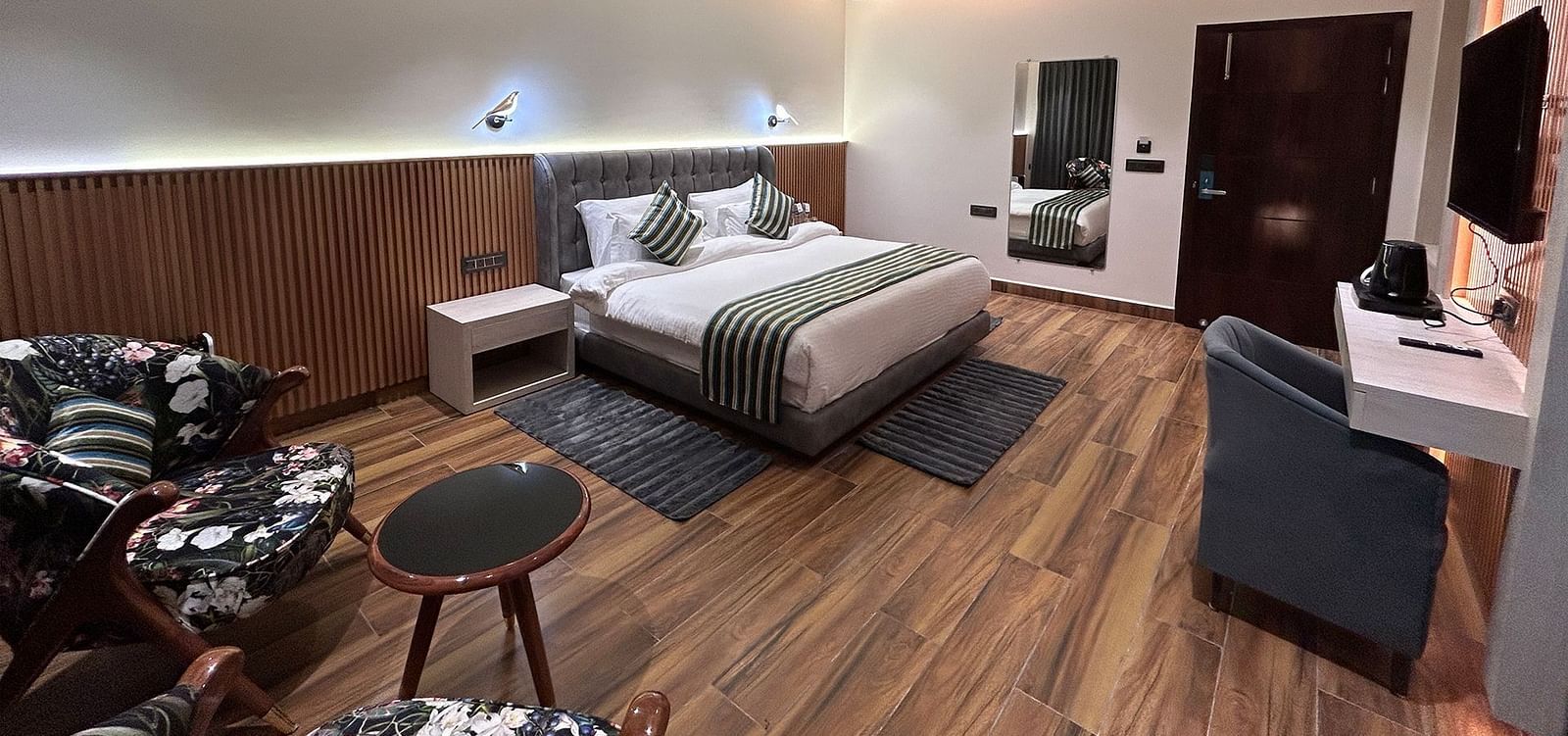 A shot of the deluxe room featuring a bed, bed side tables, two chairs, coffee table, work desk, a couch, a flat screen TV, and a full length mirror - DLS The Emerald, Nainital