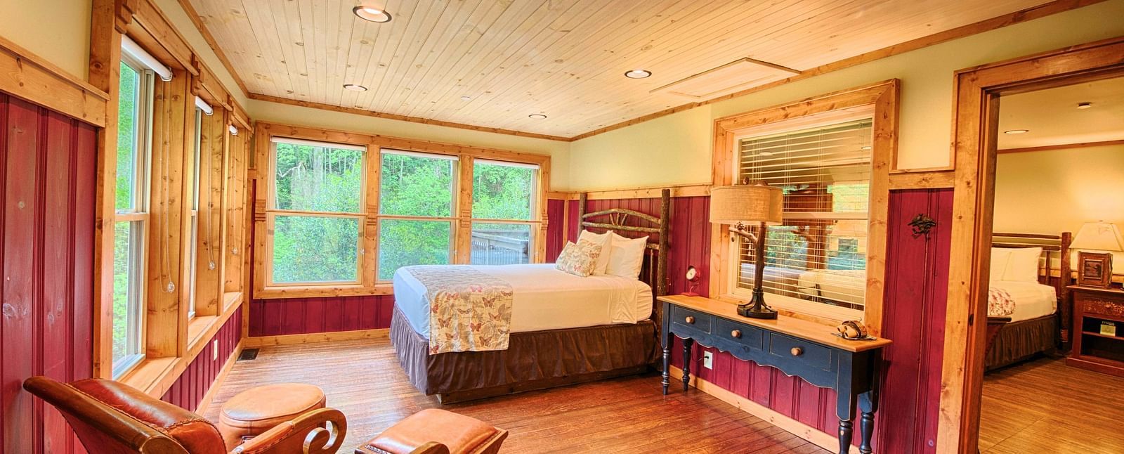 side view image of a bedroom featuring a double bed along with a cushioned armchair and a huge mirror besides it - Historic Tapoco Lodge