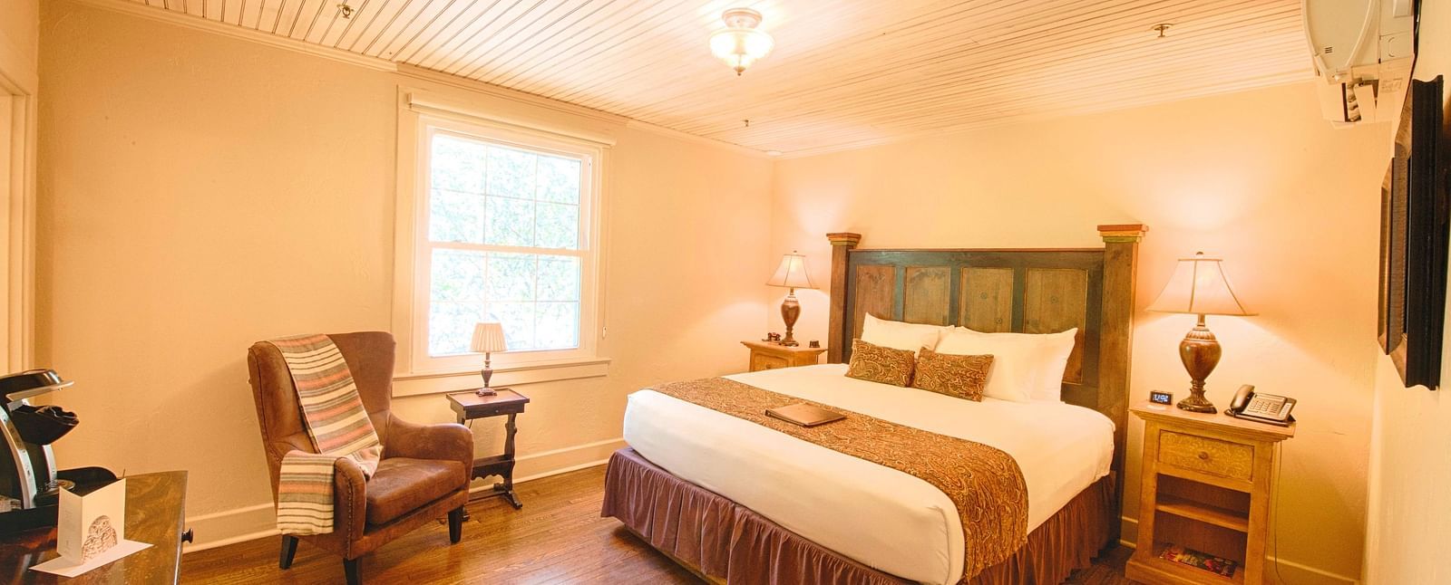 full view image of a brightly lit bedroom with a comfortable double bed with a heady headboard along with an armchair - Historic Tapoco Lodge