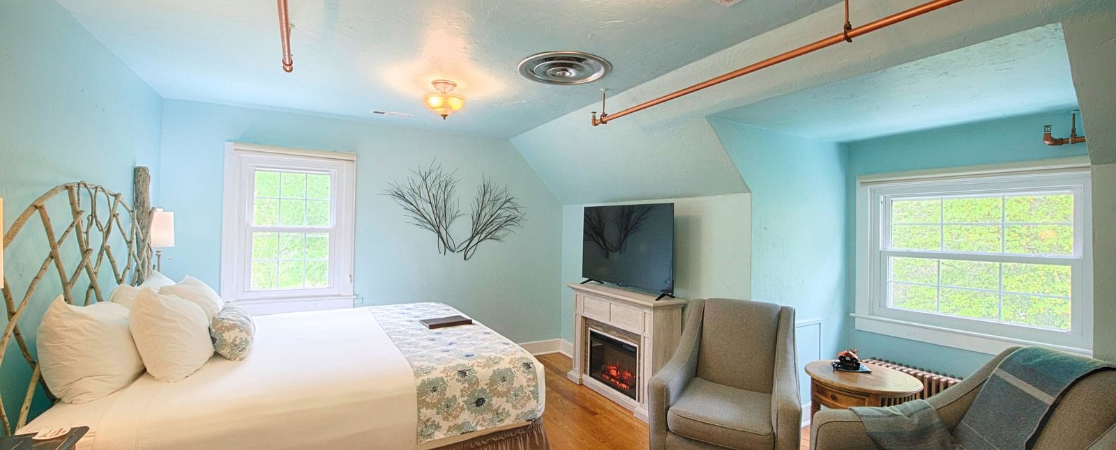 full view image of the laurel suite with pastel blue colored walls along with a flat screen television right opposite to the double bed - Historic Tapoco Lodge