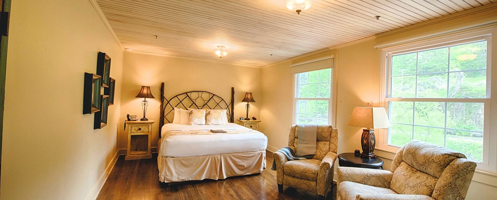 full view image of a room with wide windows featuring a cozy double bed and comfortable cushioned armchairs in front of it - Historic Tapoco Lodge