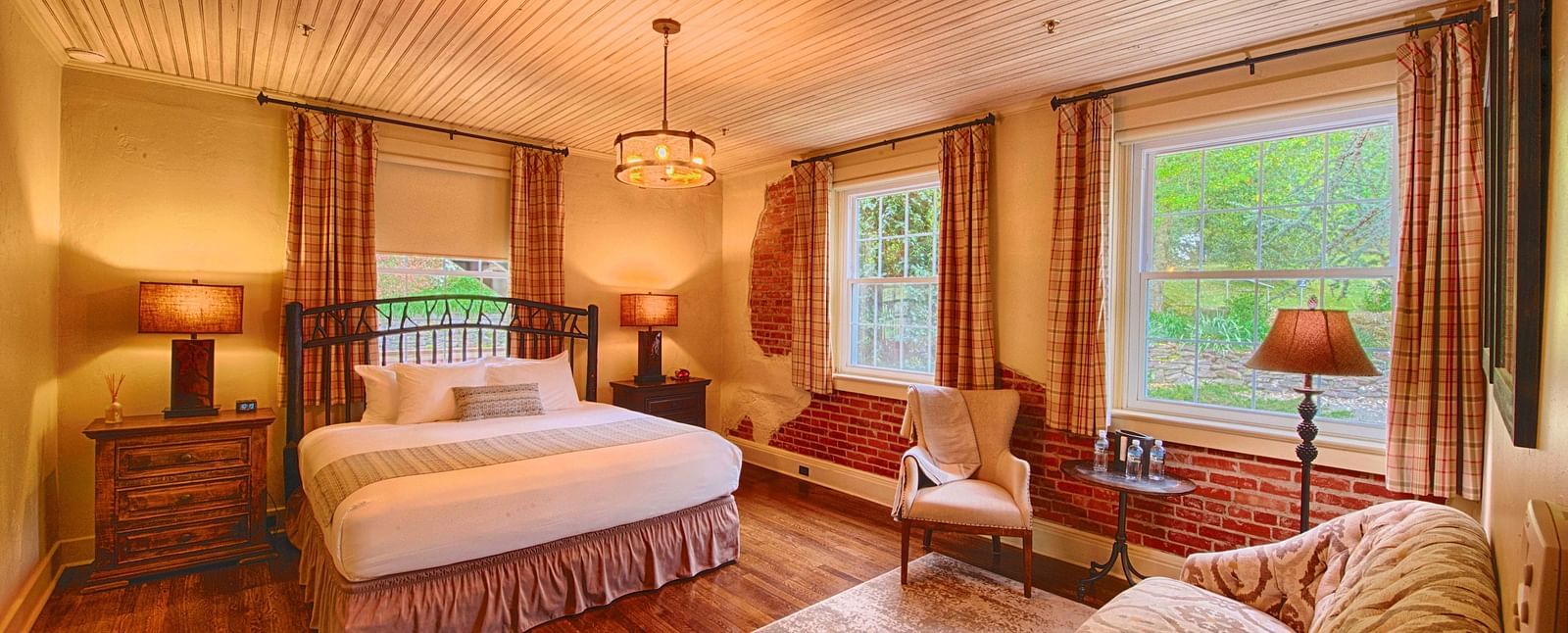 a room with ample natural lighting coming from the huge windows in the room with plush arm chairsa brightly lit bathroom featuring a door opening to the bedroom overlooking the double bed - Historic Tapoco Lodge