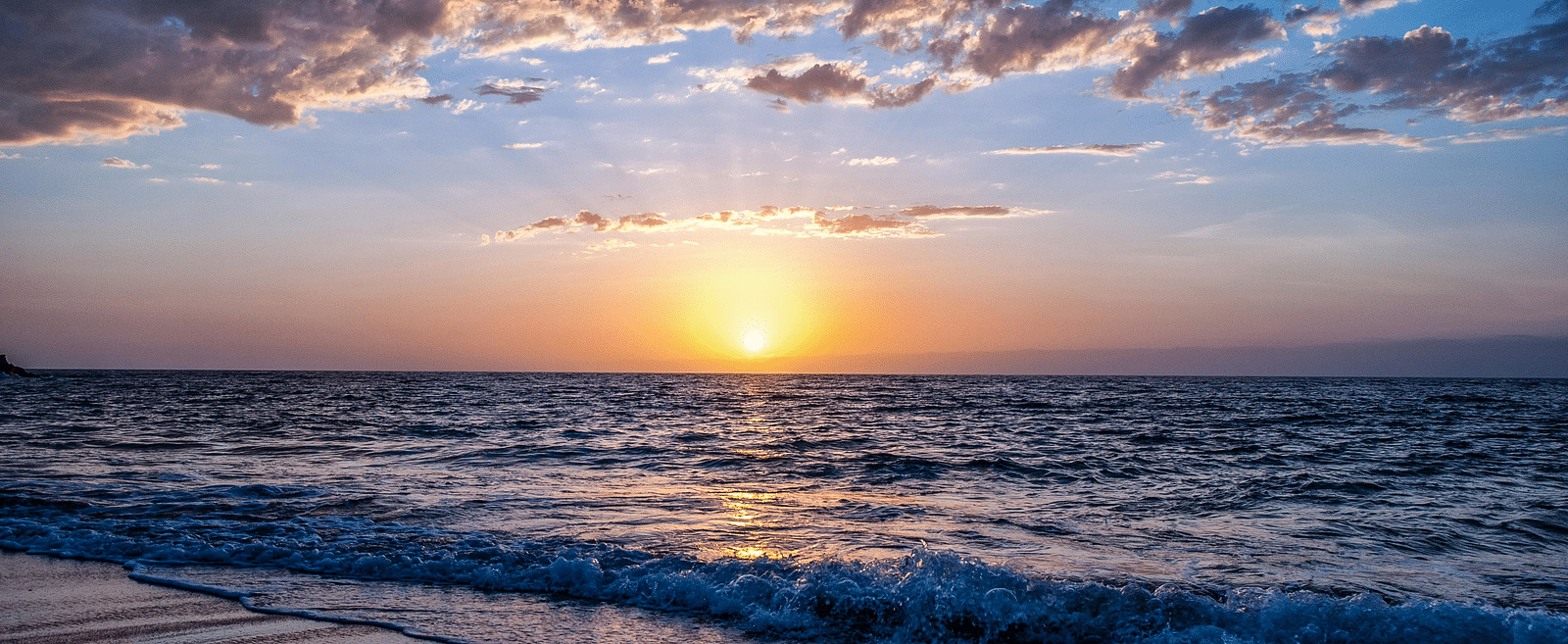 A beachfront view of the sunrise with clouds scattered across the sky.
