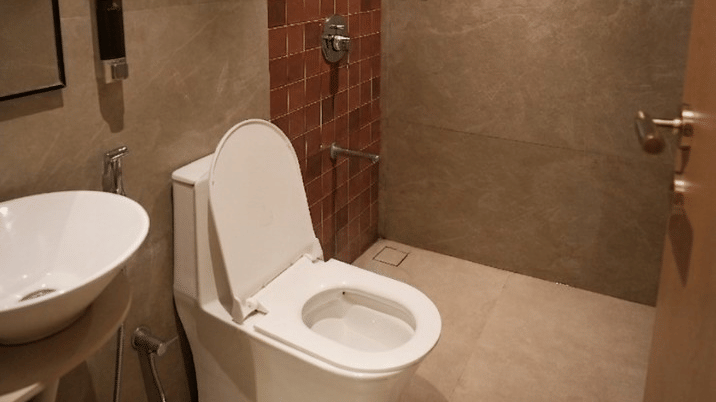 A contemporary bathroom featuring a white toilet, a wall hung washbasin, and a shower area at Bougainvillea, Alibaug.