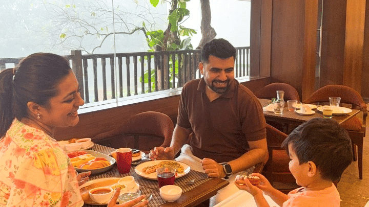 A family of three enjoying a meal together at an indoor restaurant table with a balcony view of greenery.