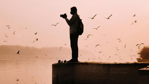An image of a photographer standing near a water body during dusk which is the perfect time for Princep Ghat photoshoot