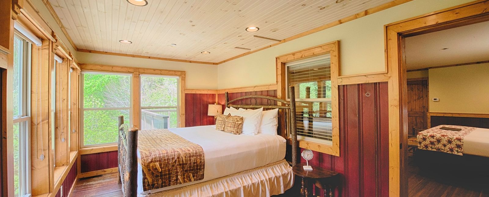 corner view image of a double bed overlooking amazing lush green views from the huge windows in front of it - Historic Tapoco Lodge