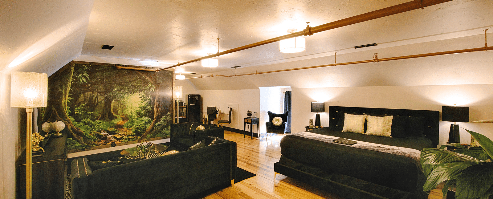 a spacious bedroom with a cozy double bed and black couch set in the common seating area with a jungle mastiff made in the feature wall of the suite - Historic Tapoco Lodge