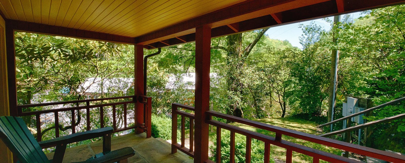 a beautiful wooden porch with chairs kept on it facing towards the green forests - Historic Tapoco Lodge