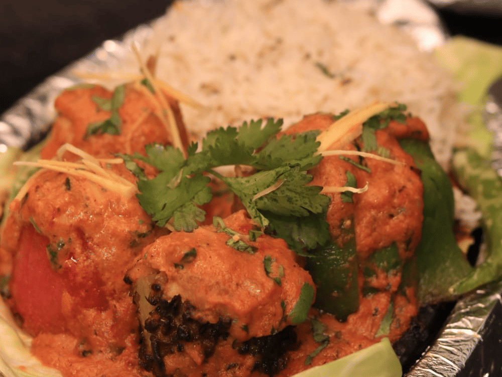 A plate of flavorful rice and juicy tandoori prawns garnished with fresh coriander, served hot at Papaya Tree Hotels.