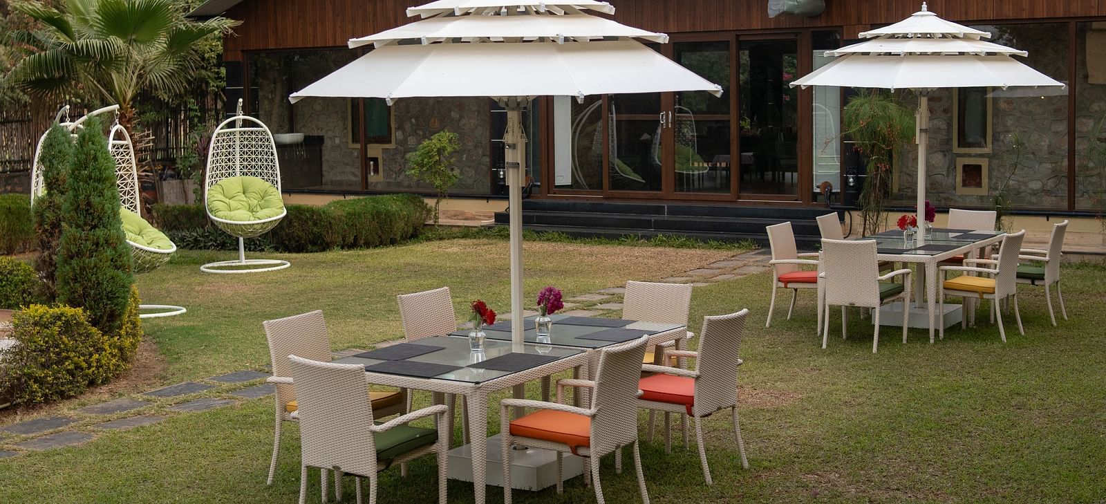 An outdoor seating area at Aamaghati Jungle Retreat Ranthambore with white umbrellas and hanging swing chairs.