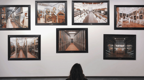 a girl sitting on a bench looking at the paintings hung inside a museum