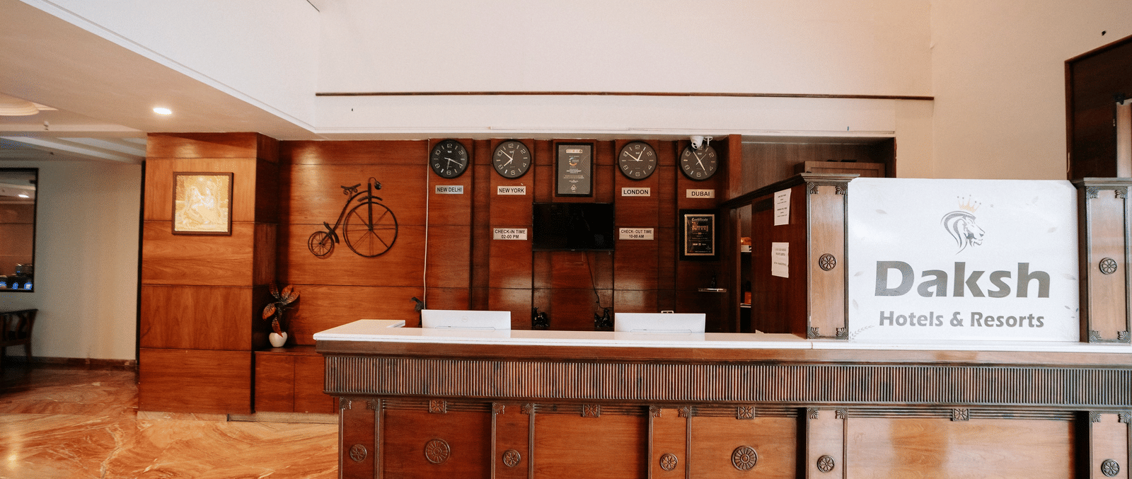 The hotel reception desk with a dark wood finish and a marble-effect floor at Daksh The Madhuvan Suites, Dwarka.