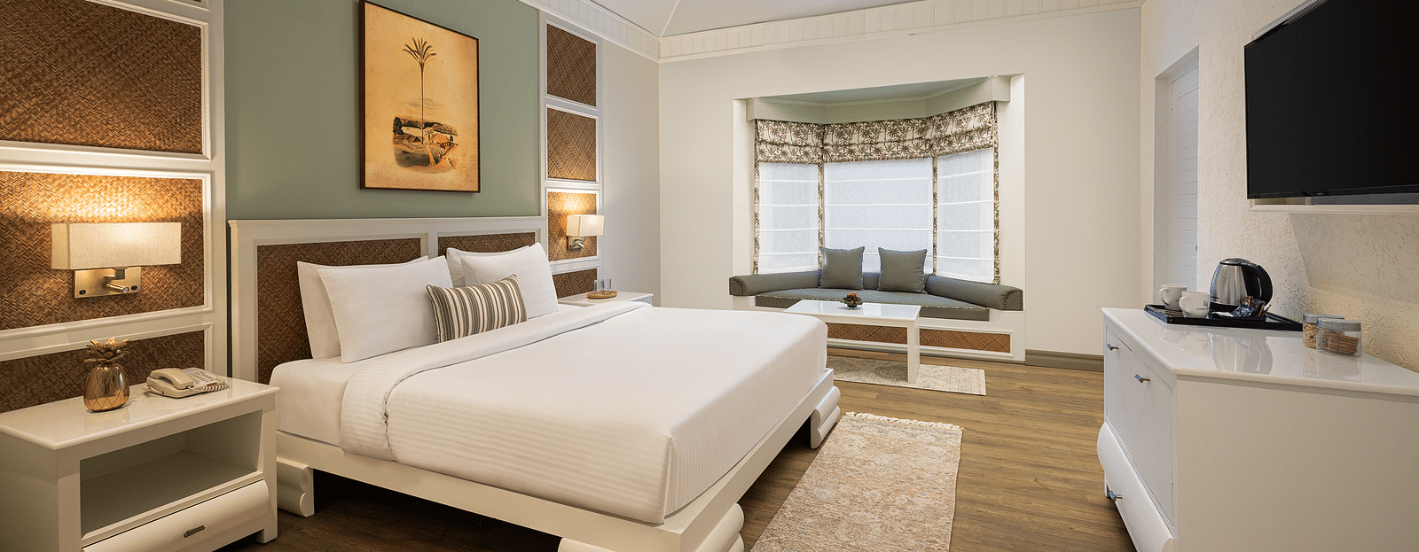 An image of a bedroom with double size bed, bedside table on either side, photos hanged on the wall and four windows from which natural lights are coming in - The Riverview Retreat,  Corbett