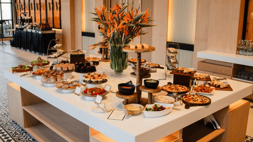 A grand table in the center of the dining space, arranged with different items for a buffet