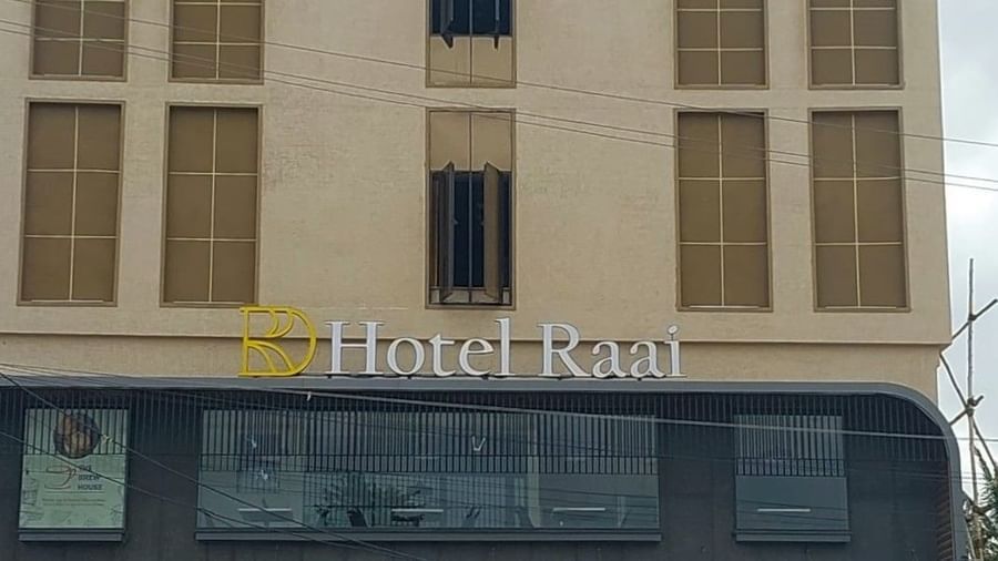 Facade of Hotel Raai, Hosur featuring four storey building. The ground floor has glass walls at the entrance and the other floors have concrete walls with long windows facing the street.