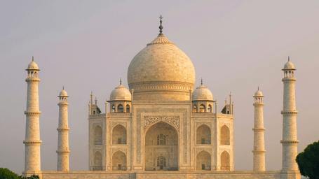 Facade of the Taj Mahal illuminated in golden hues with its reflection on the water in the front