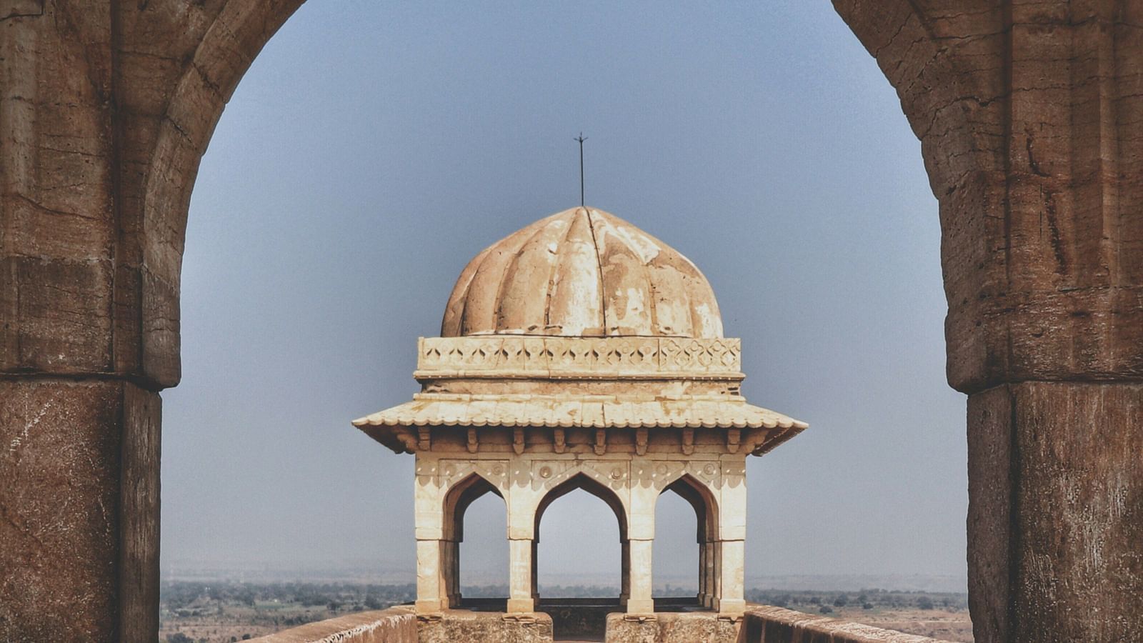 An archway frames a distant dome structure on a clear day, capturing the essence of serene architectural beauty.