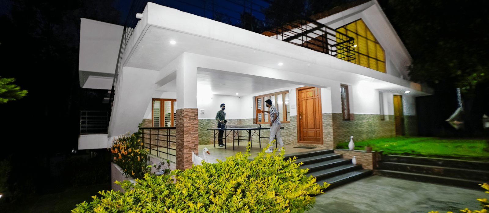 Facade view of WOW Bungalow, Yercaud, with two people playing table tennis on the porch.