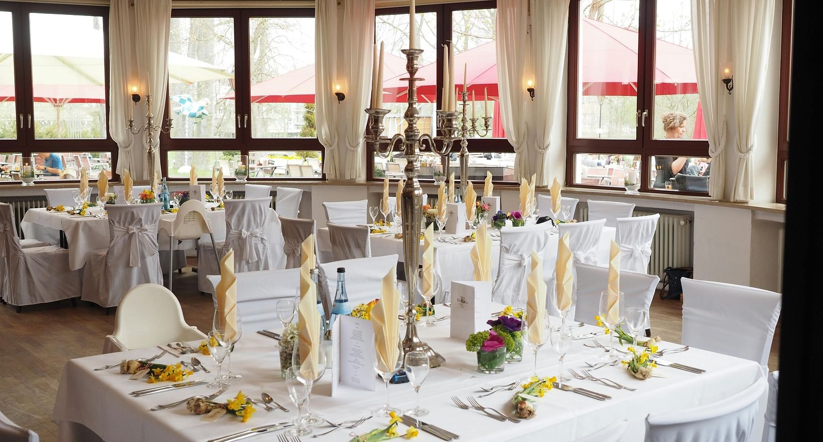 A banquet hall set up with multiple tables draped in white linens and decorated with floral centrepieces, candles, and elegant place settings